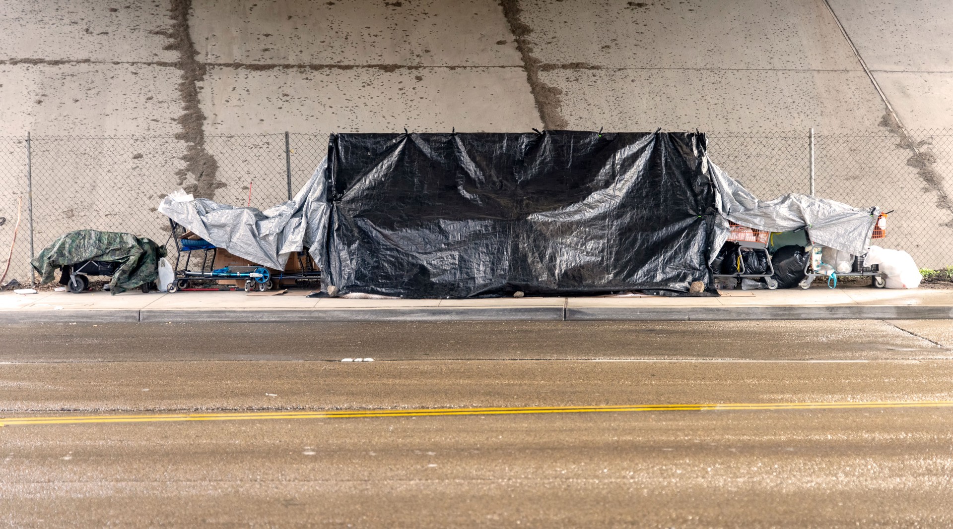 A homeless camp with a black tarp under a bridge during a rain storm