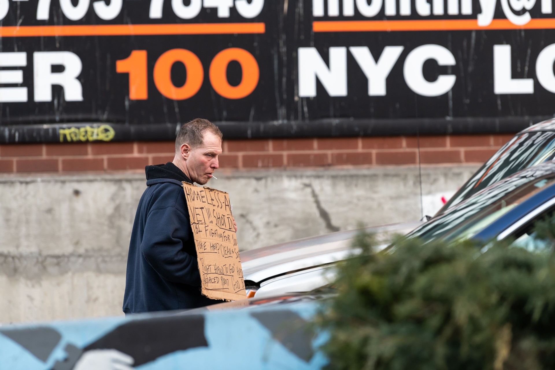 Manhattan, New York City sidewalk with homeless man veteran beggar asking for money walking by cars