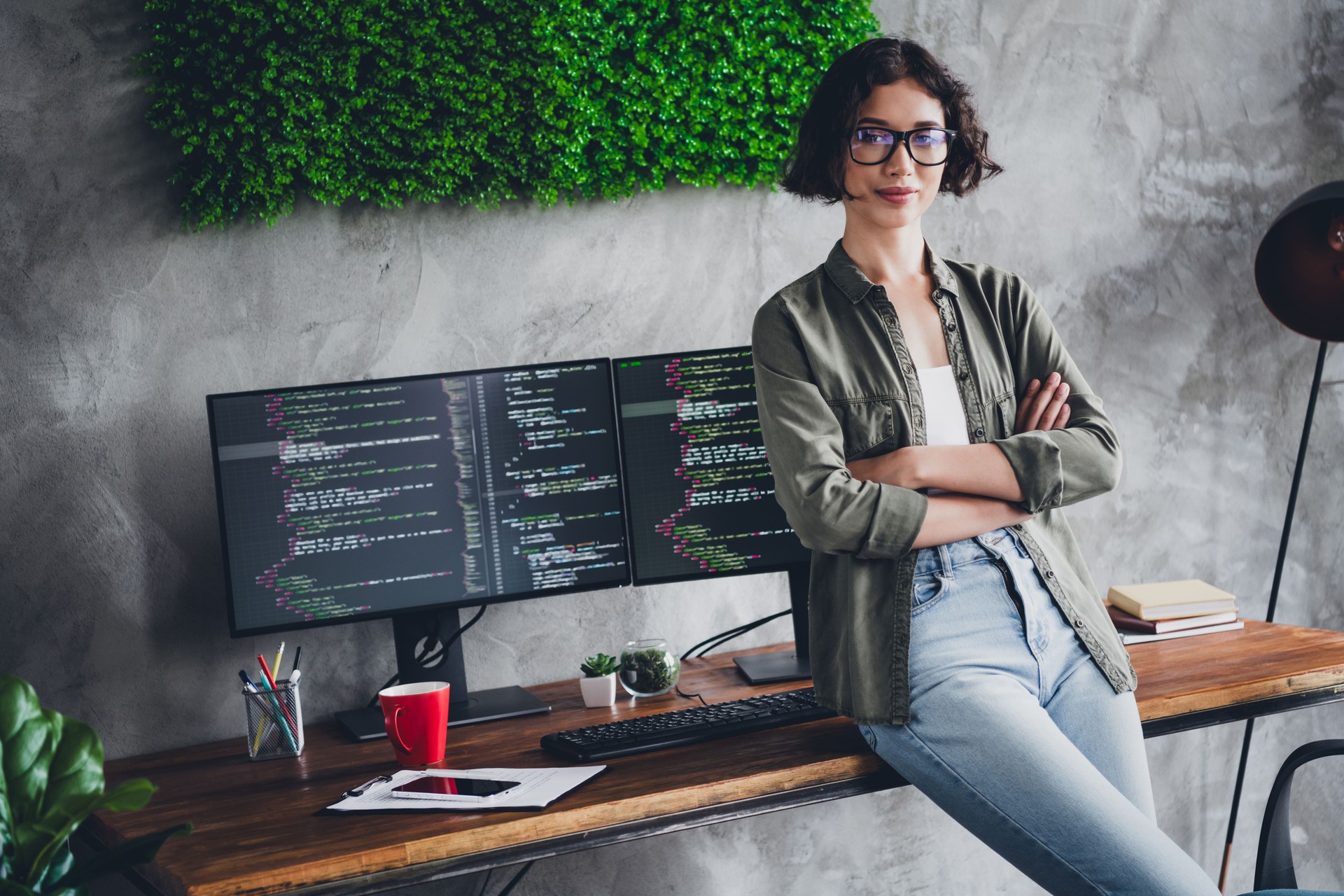 Confident female programmer working from a modern workspace with dual monitors displaying source code